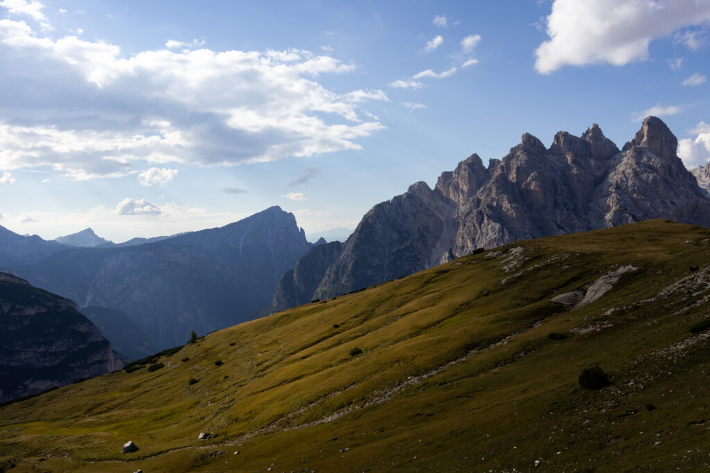 Scenic mountain view in the Alps with a clear blue sky, grassy field in the foreground, and mountains in the background.