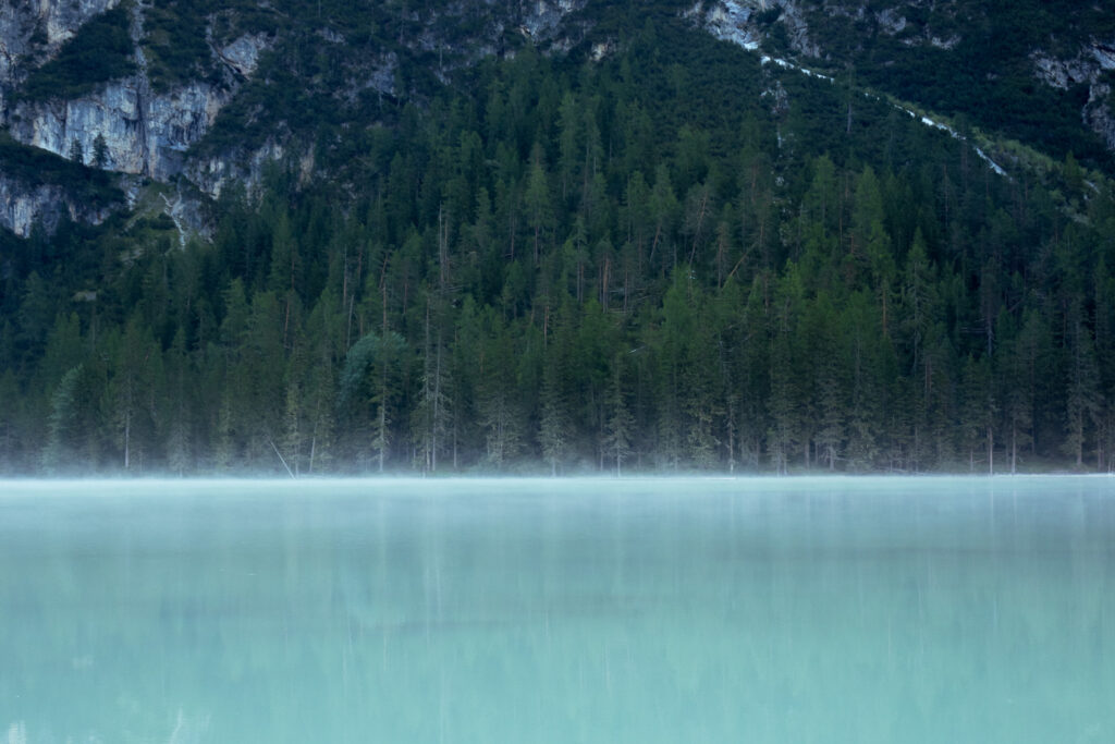 Close-up of turquoise water with a hint of fog above it, mountains and forest in the background.