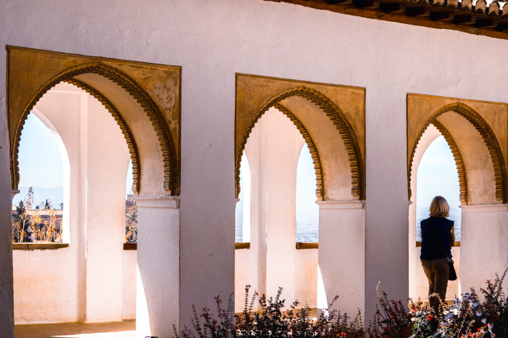 Woman standing by the rightmost of three archways, looking at the view in soft white and golden light