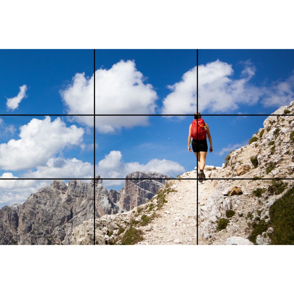 A woman with a red backpack hiking in the Alps, with a blue sky and mountains in the background. Rule of Thirds.